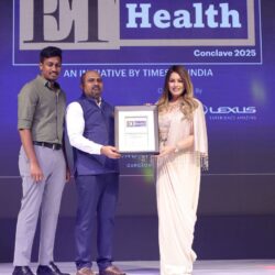 Three individuals on stage at the ET Health Conclave 2025 award ceremony, with one holding a framed award. The backdrop features the event logo, "ET Health" and "Conclave 2025," along with the Lexus sponsorship branding. The scene is illuminated with purple and blue lighting.
