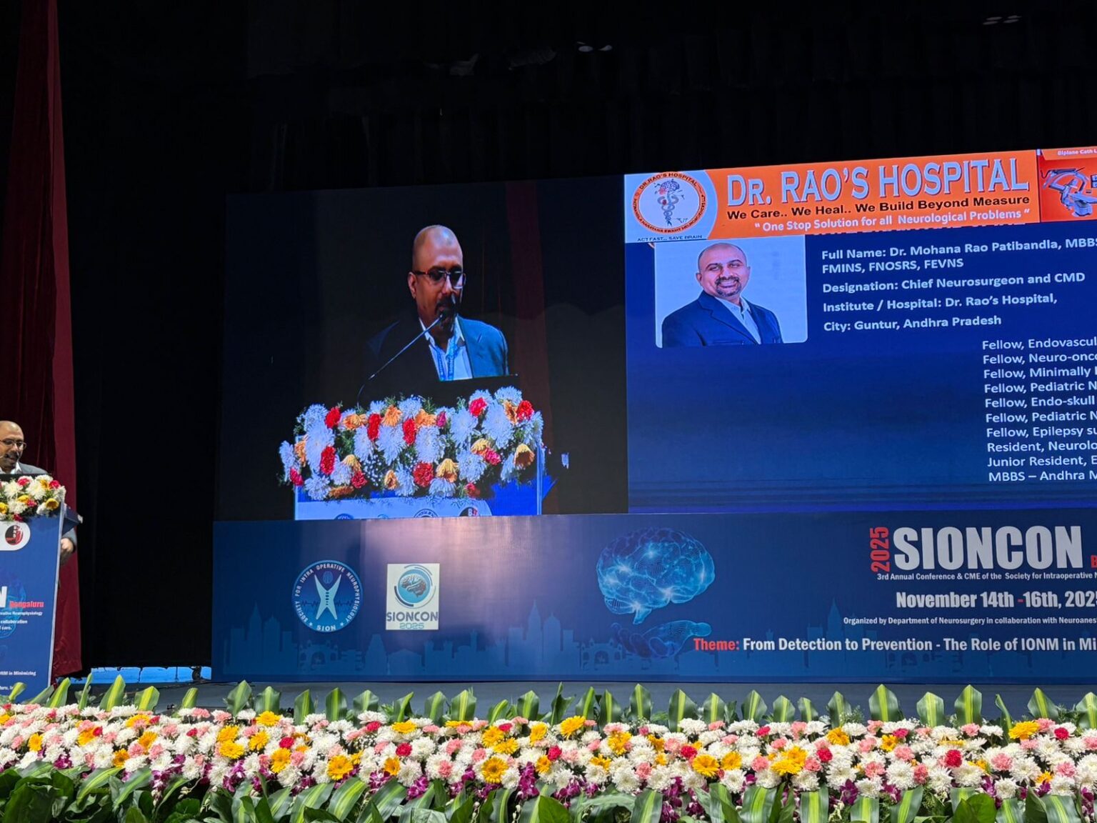 Dr. Mohana Rao Patibandla standing at the podium at SIONCON 2025 in Bengaluru, with a large screen displaying his professional profile, qualifications, and fellowships from leading global neurosurgery centers.